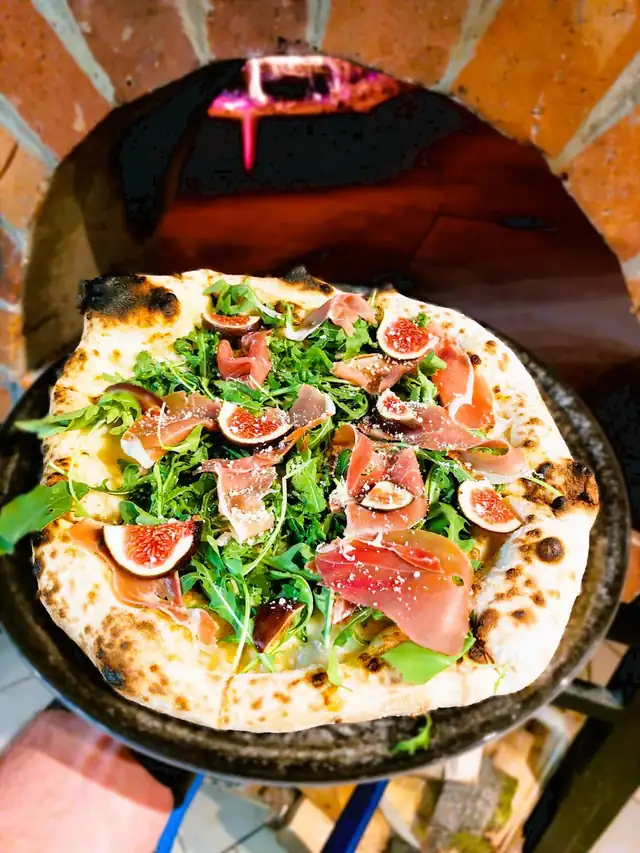 Pizza z rukolą i figami przed ceglanym wylotem pieca opalanego drewnem w FARICO